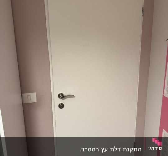 דלת לבנה עם ידית כסופה על קיר ורוד